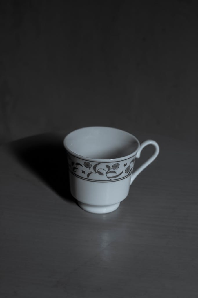 A close-up of a patterned ceramic cup on a shadowy table, showcasing minimalist design.