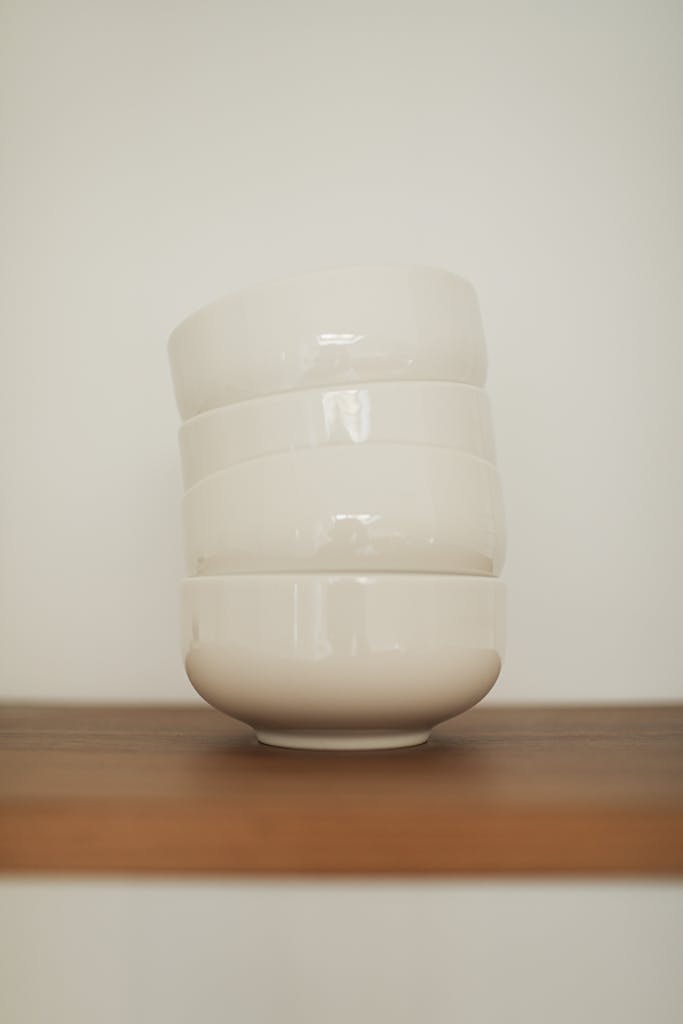 Elegant stack of white ceramic bowls on a wooden shelf, ideal for minimalist kitchen decor.