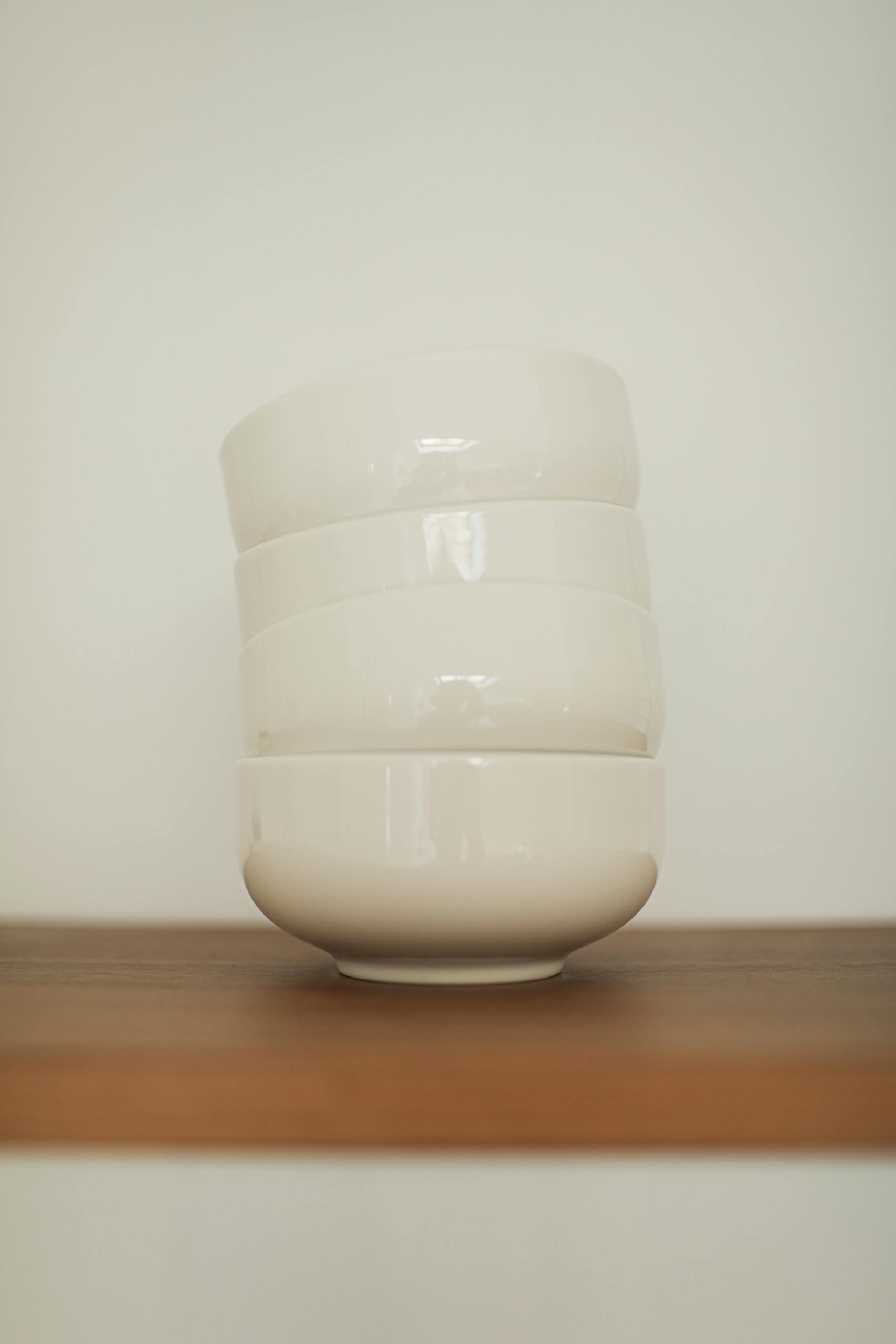 Elegant stack of white ceramic bowls on a wooden shelf, ideal for minimalist kitchen decor.